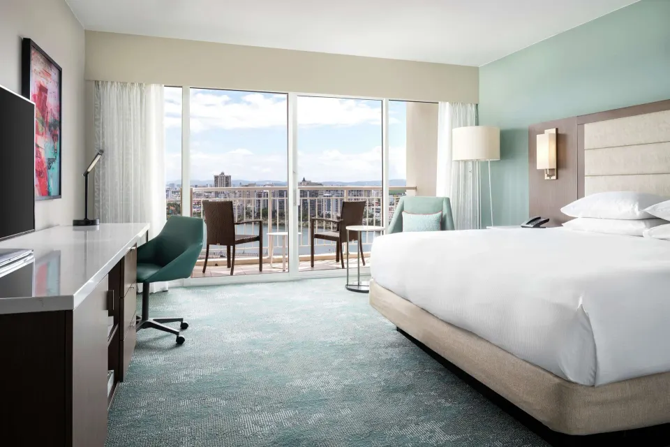 King guest room with desk, balcony chairs, and bright windows at Caribe Hilton.