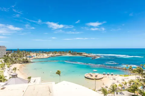 High-floor ocean view from a Corner Suite at Caribe Hilton, overlooking beach, lagoon and turquoise water.