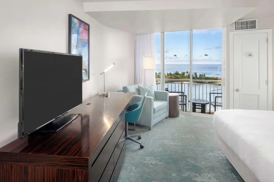 Caribe Hilton corner suite bedroom with a king bed, TV console, desk, armchair and ocean-view balcony.