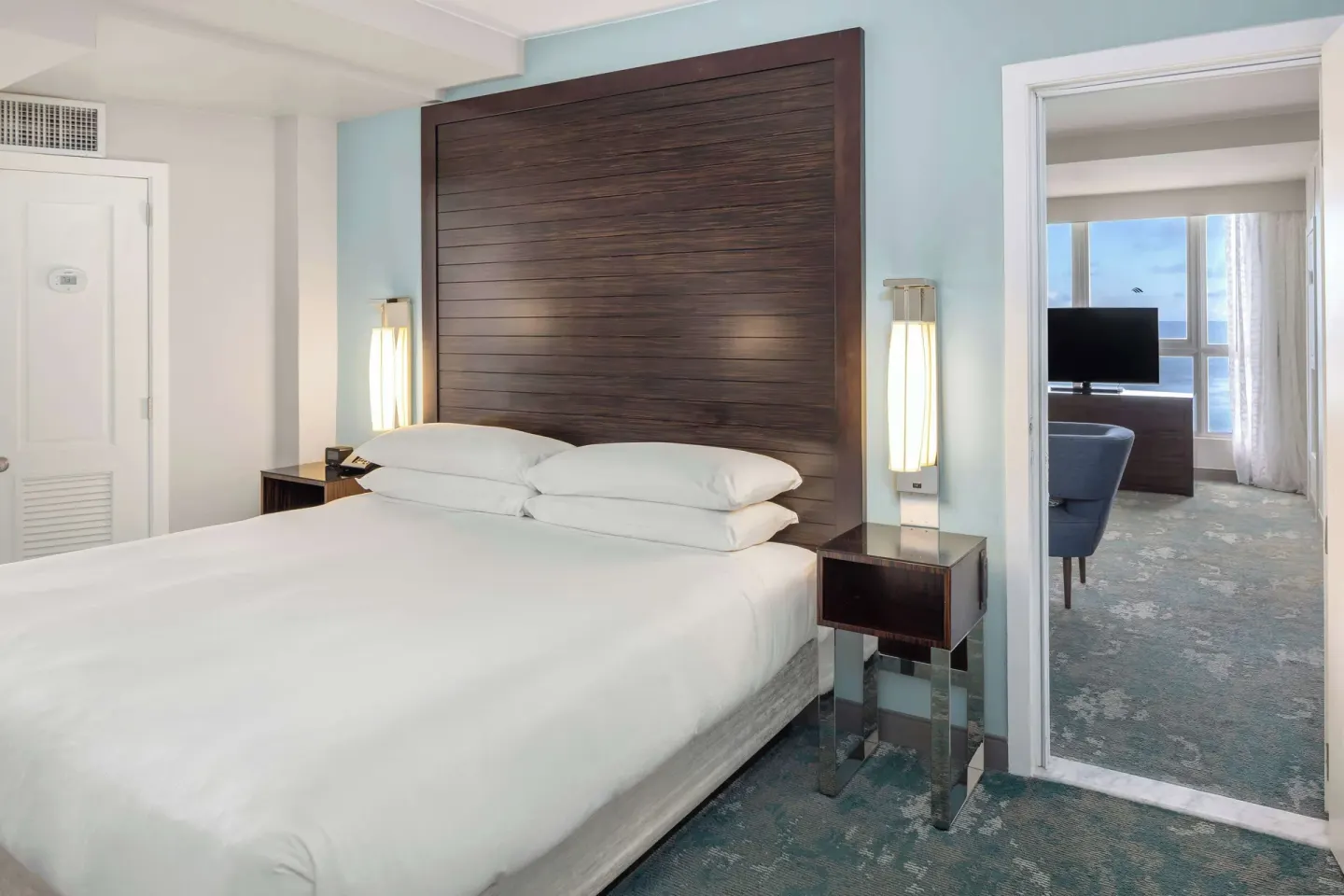 King bed in a Caribe Hilton corner suite bedroom with the ocean visible through the next room.