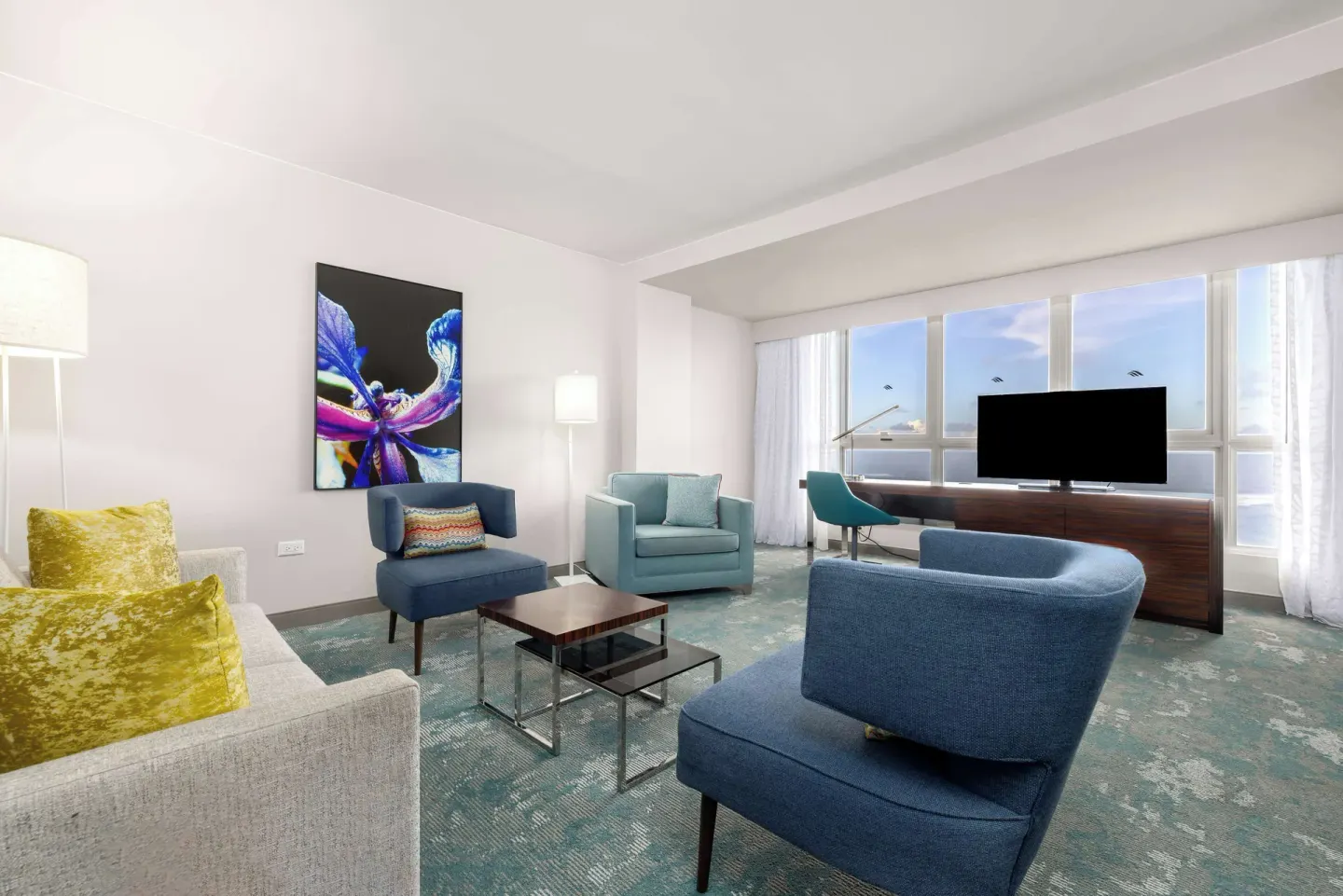 Living room of a Caribe Hilton corner suite with sofas, blue chairs, TV and ocean-facing windows.