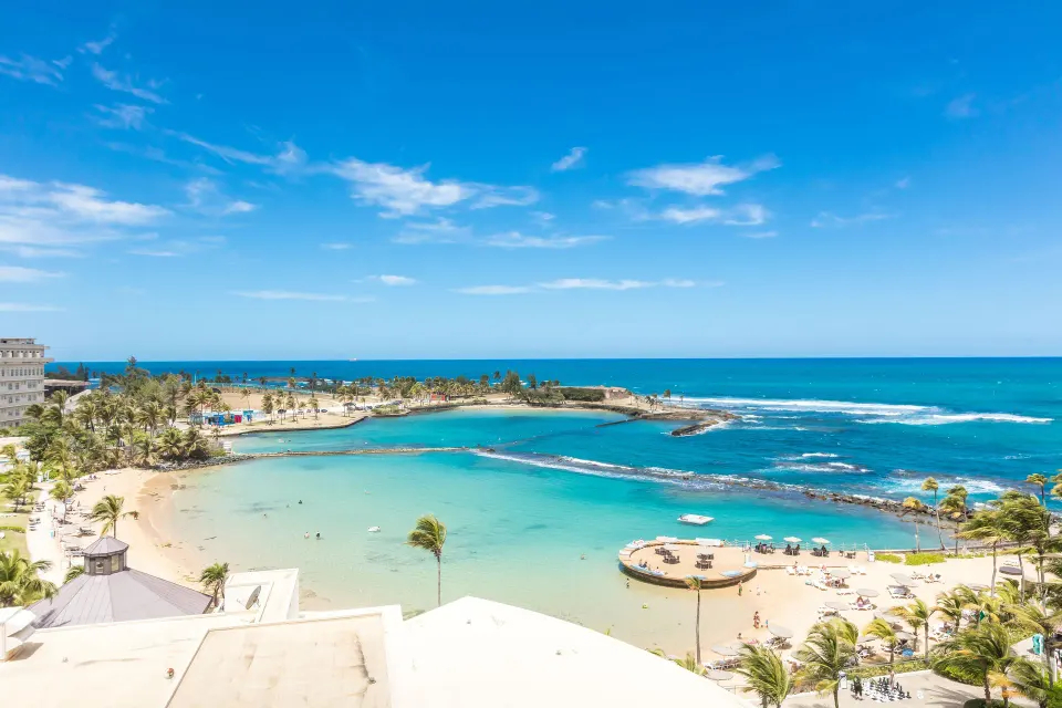 Ocean and beach view from a high-floor corner suite at Caribe Hilton overlooking turquoise water.
