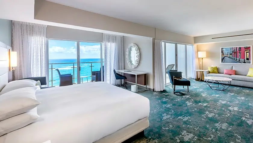 Family room with king bed, sitting area, balcony, and ocean view at Caribe Hilton.