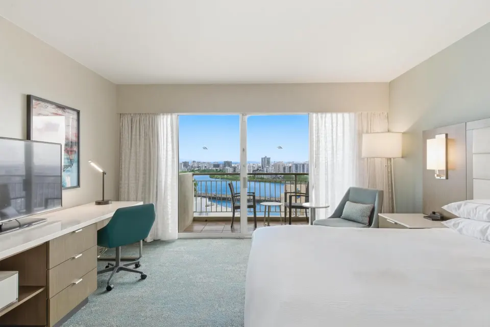 Family Room Ocean View king bed facing balcony with water and city views at Caribe Hilton.