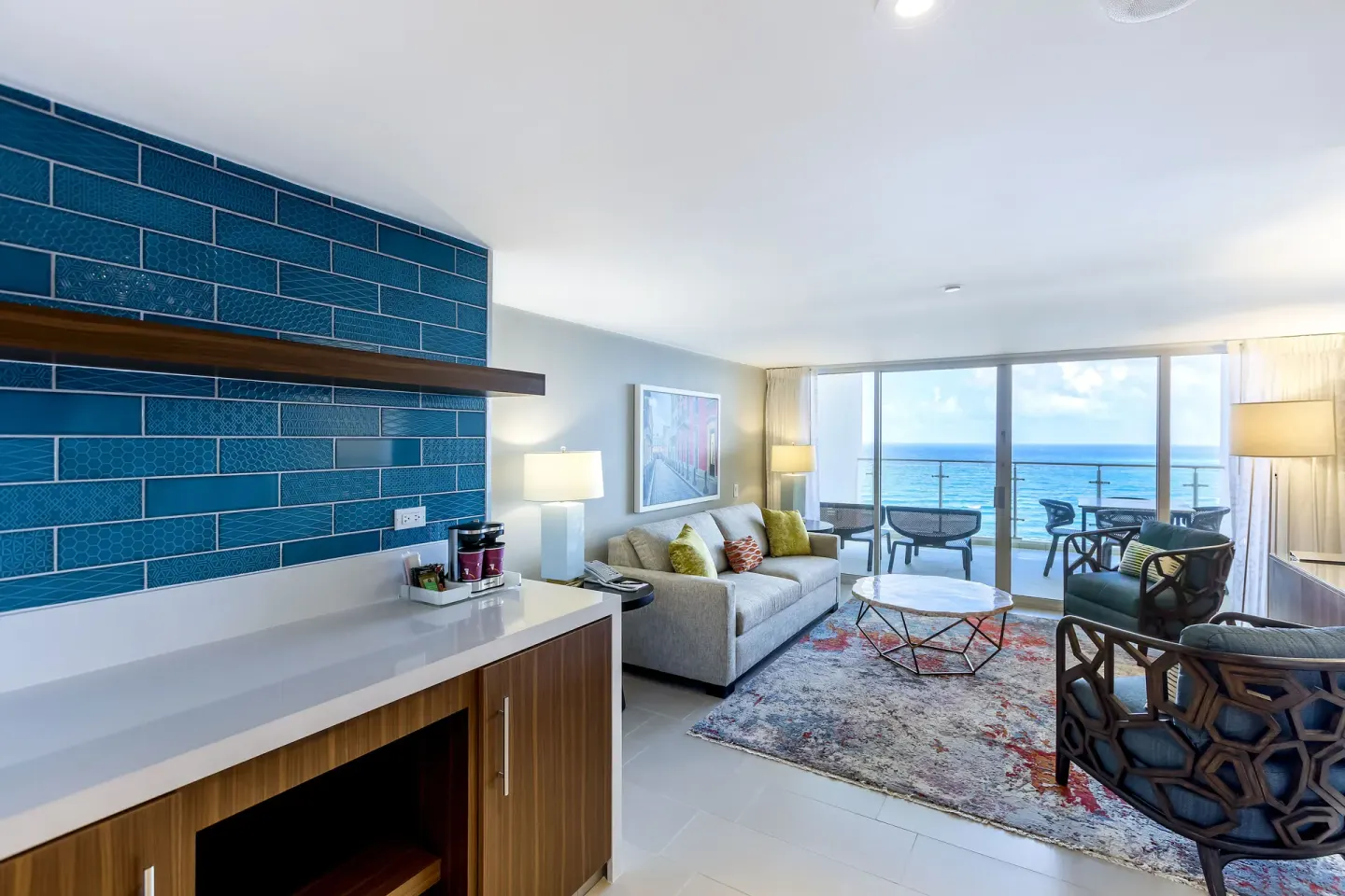Suite living room with sofa, chairs, blue tile wall, and ocean balcony at Caribe Hilton.