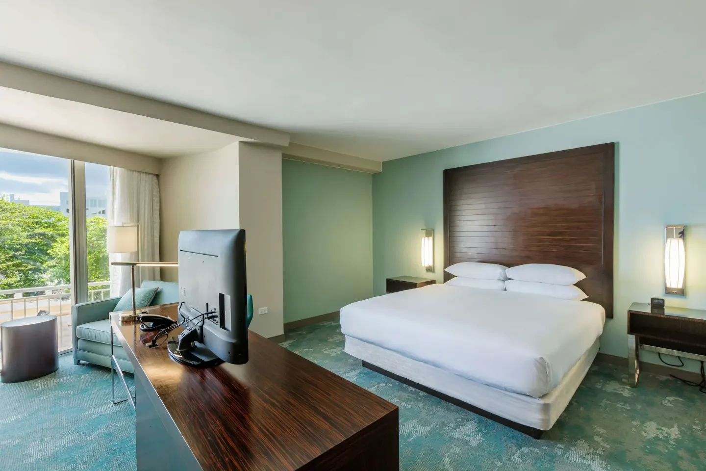 Junior Suite king bed, desk, chair, and balcony window at Caribe Hilton.