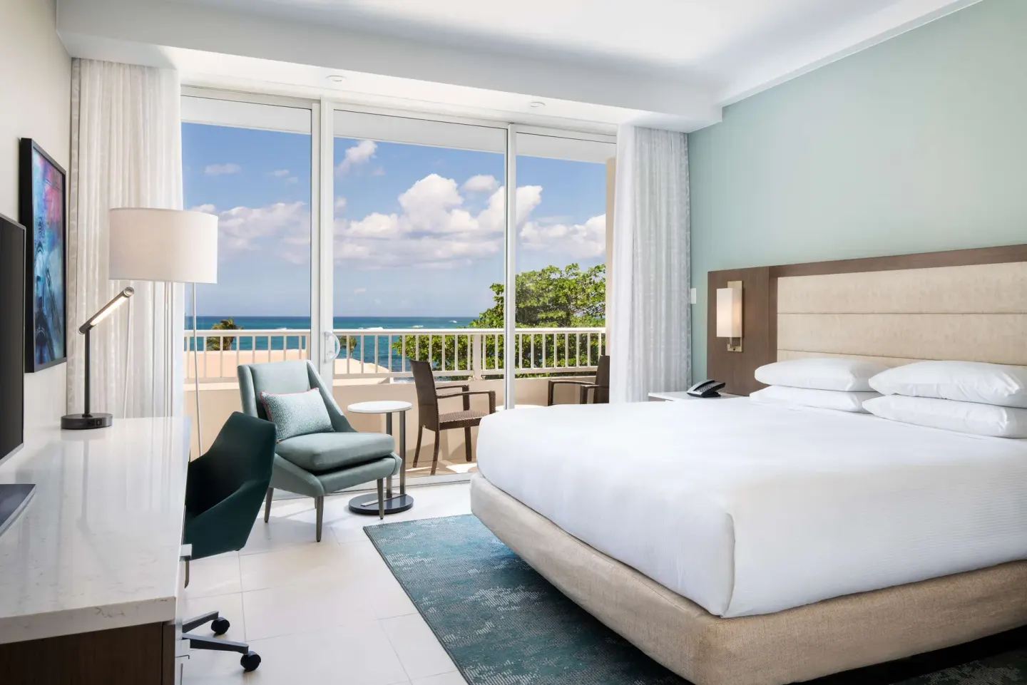 Junior Suite king bed beside balcony doors with ocean view at Caribe Hilton.