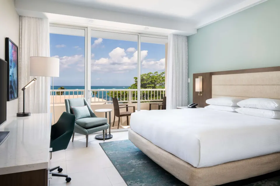 Junior Suite king bed beside balcony doors with ocean view at Caribe Hilton.
