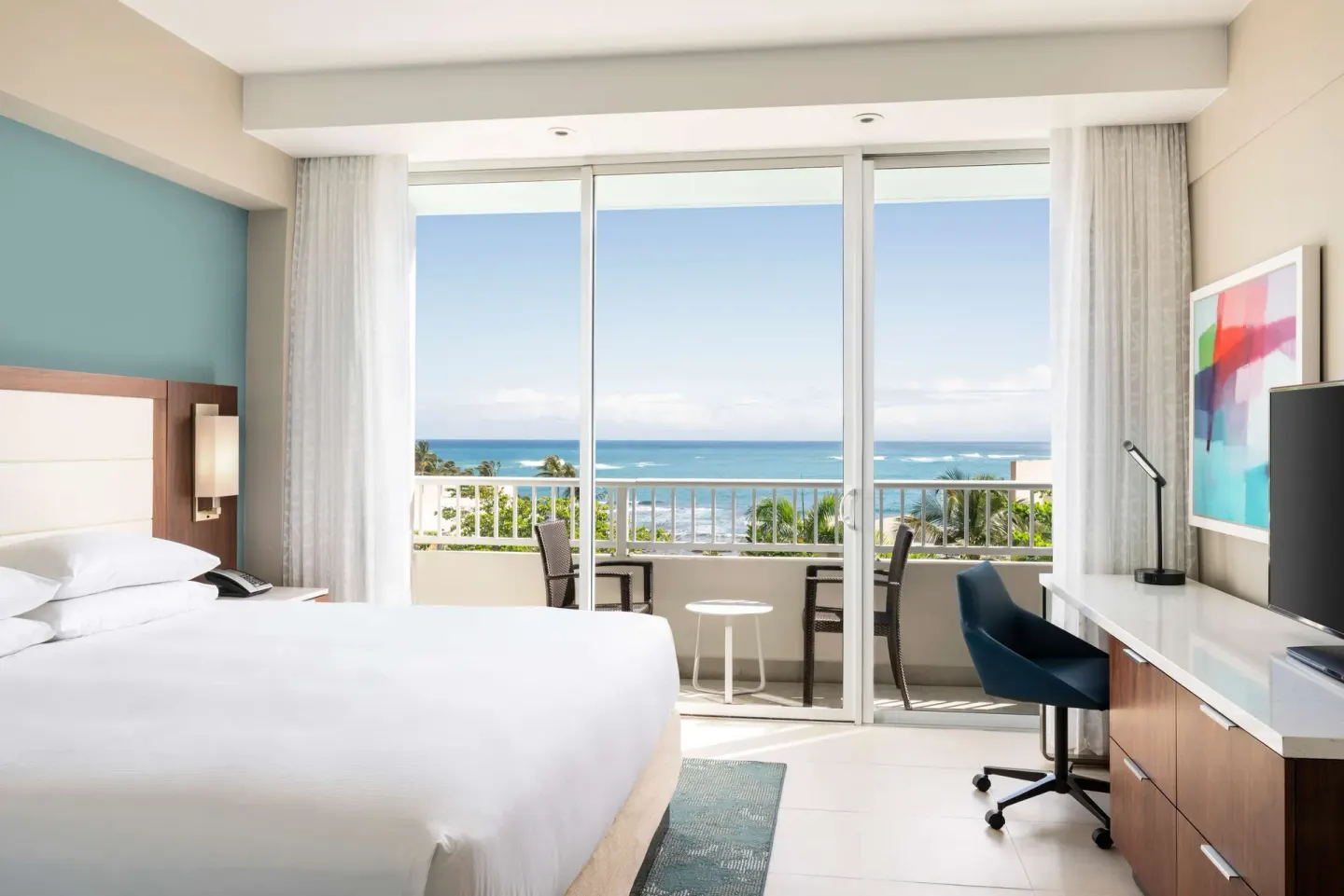 Premium king suite bedroom at Caribe Hilton with balcony seating and a wide ocean-facing window.