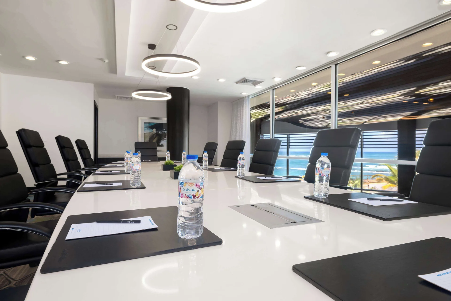 A boardroom table with black chairs, notebooks, and water bottles at Caribe Hilton.