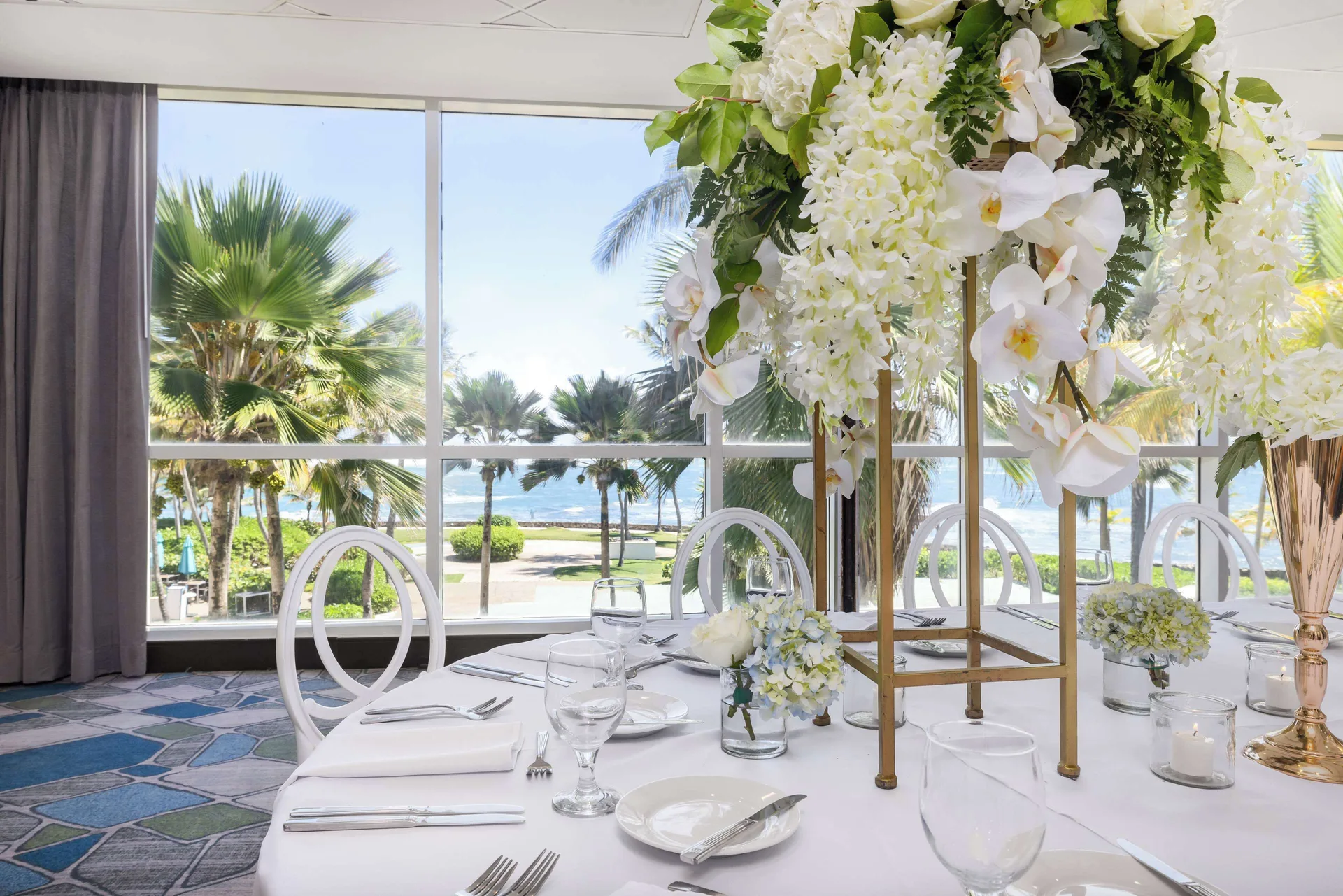 Event table with white floral centerpiece and ocean-facing windows at Caribe Hilton.