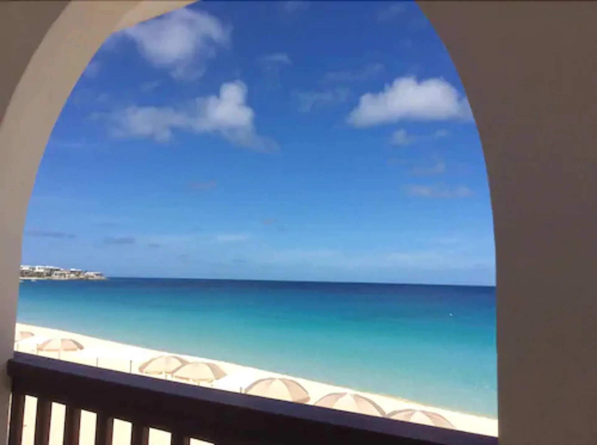 Arched balcony frames a turquoise ocean and beach umbrellas at Carimar Beach Club.