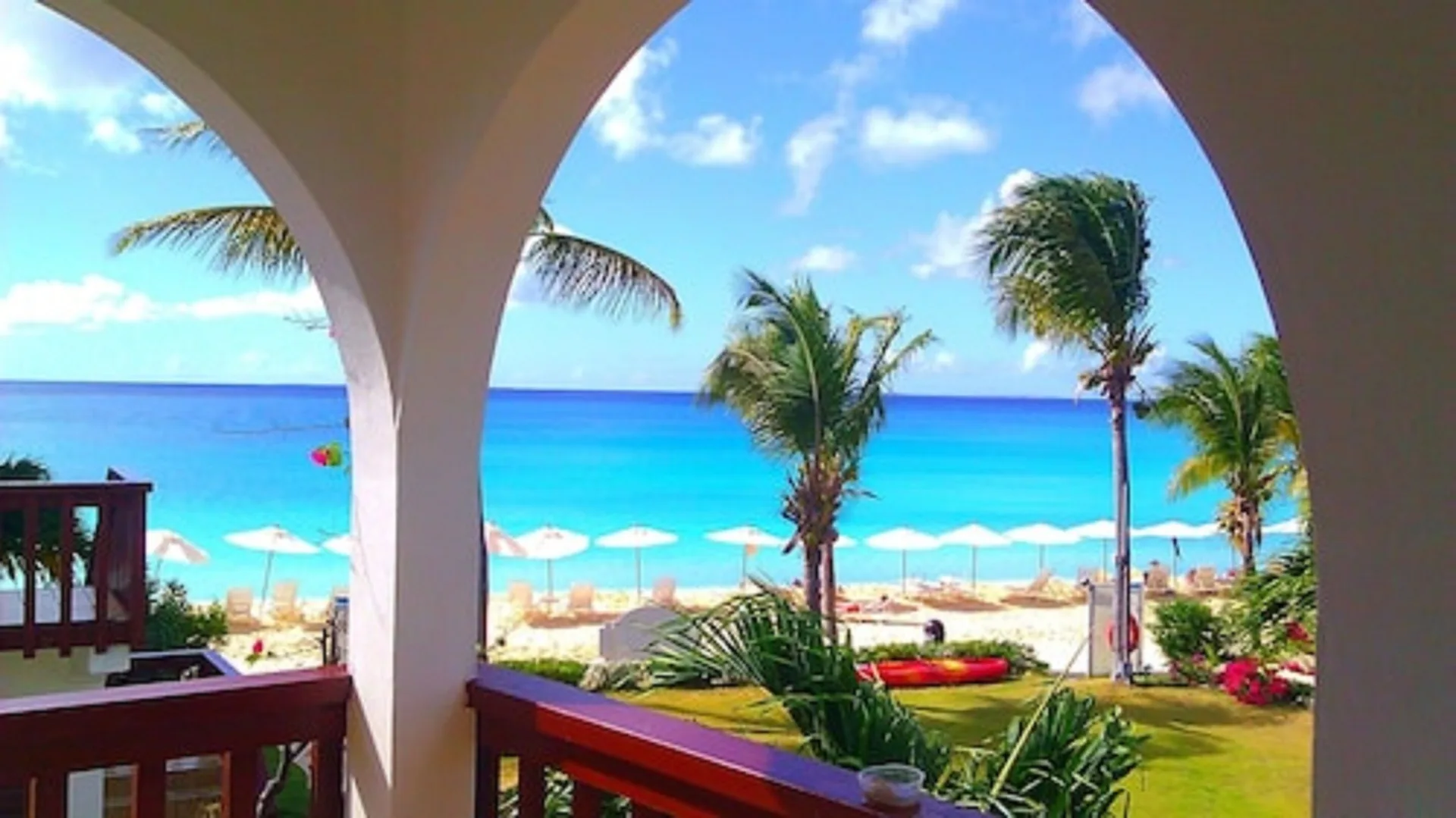 Balcony arches overlook palms, beach umbrellas, and blue sea at Carimar Beach Club.