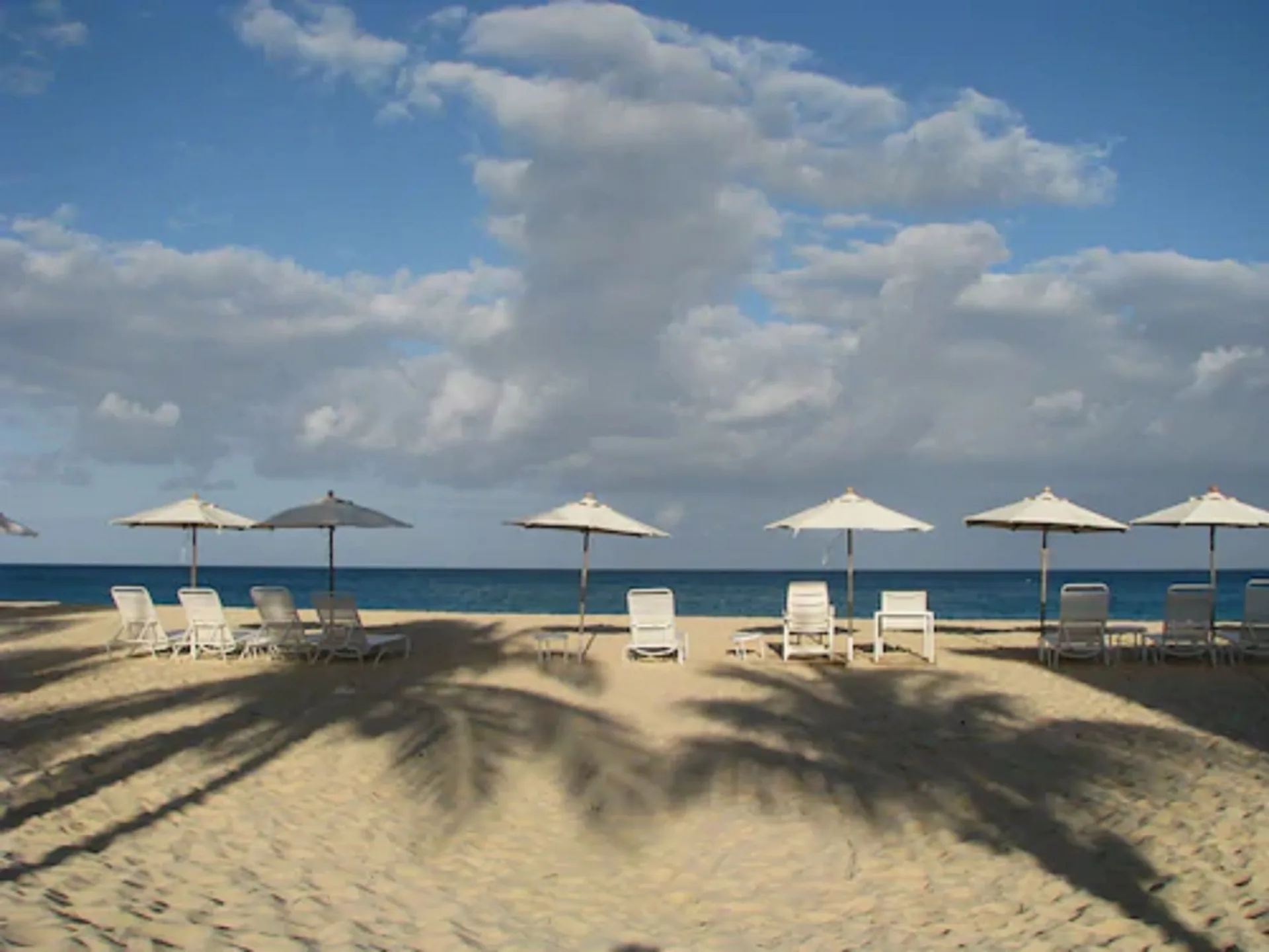 Beach loungers and umbrellas face the ocean under a cloudy sky at Carimar Beach Club.