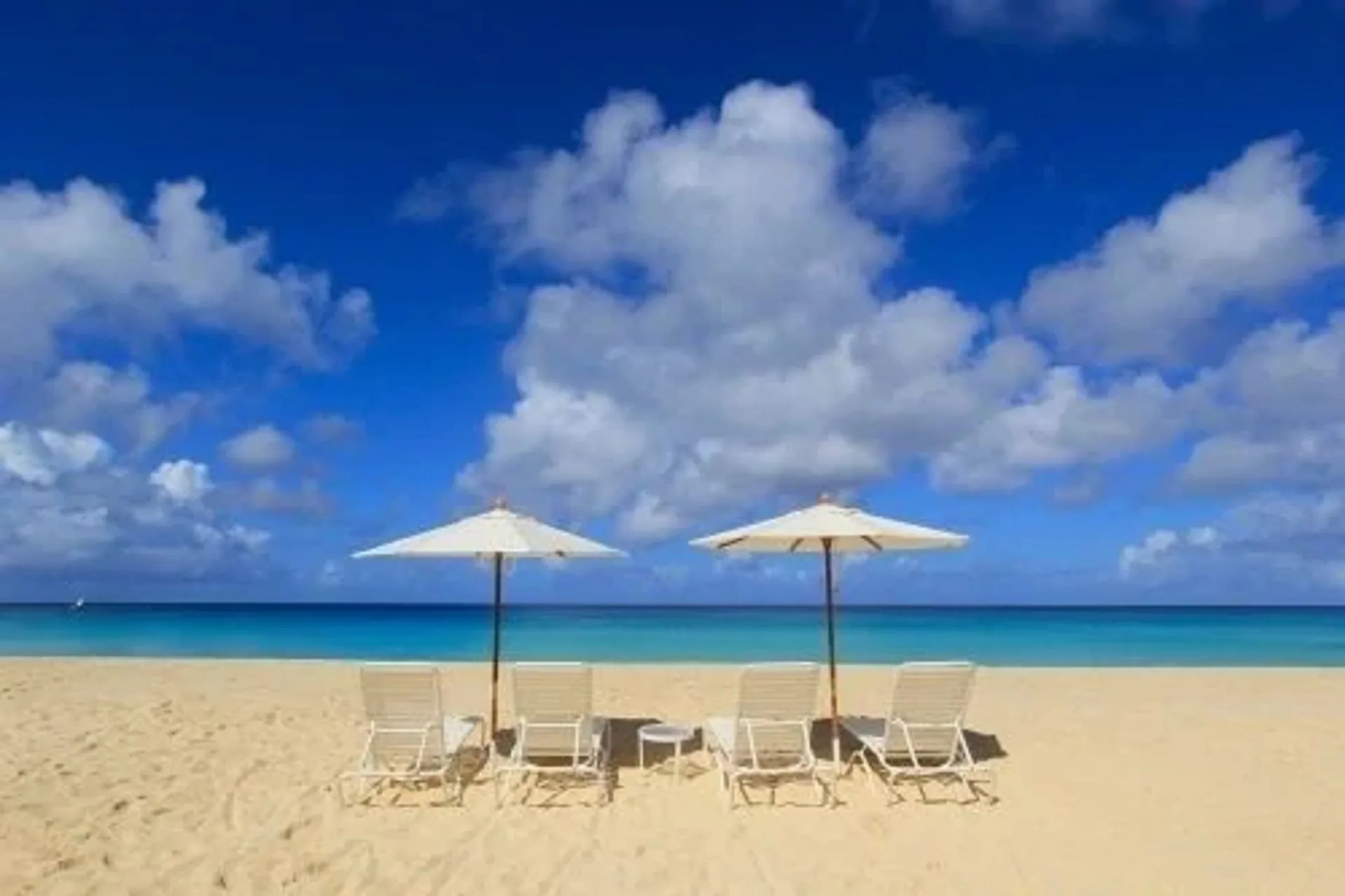 Two beach umbrellas with lounge chairs on open sand at Carimar Beach Club.