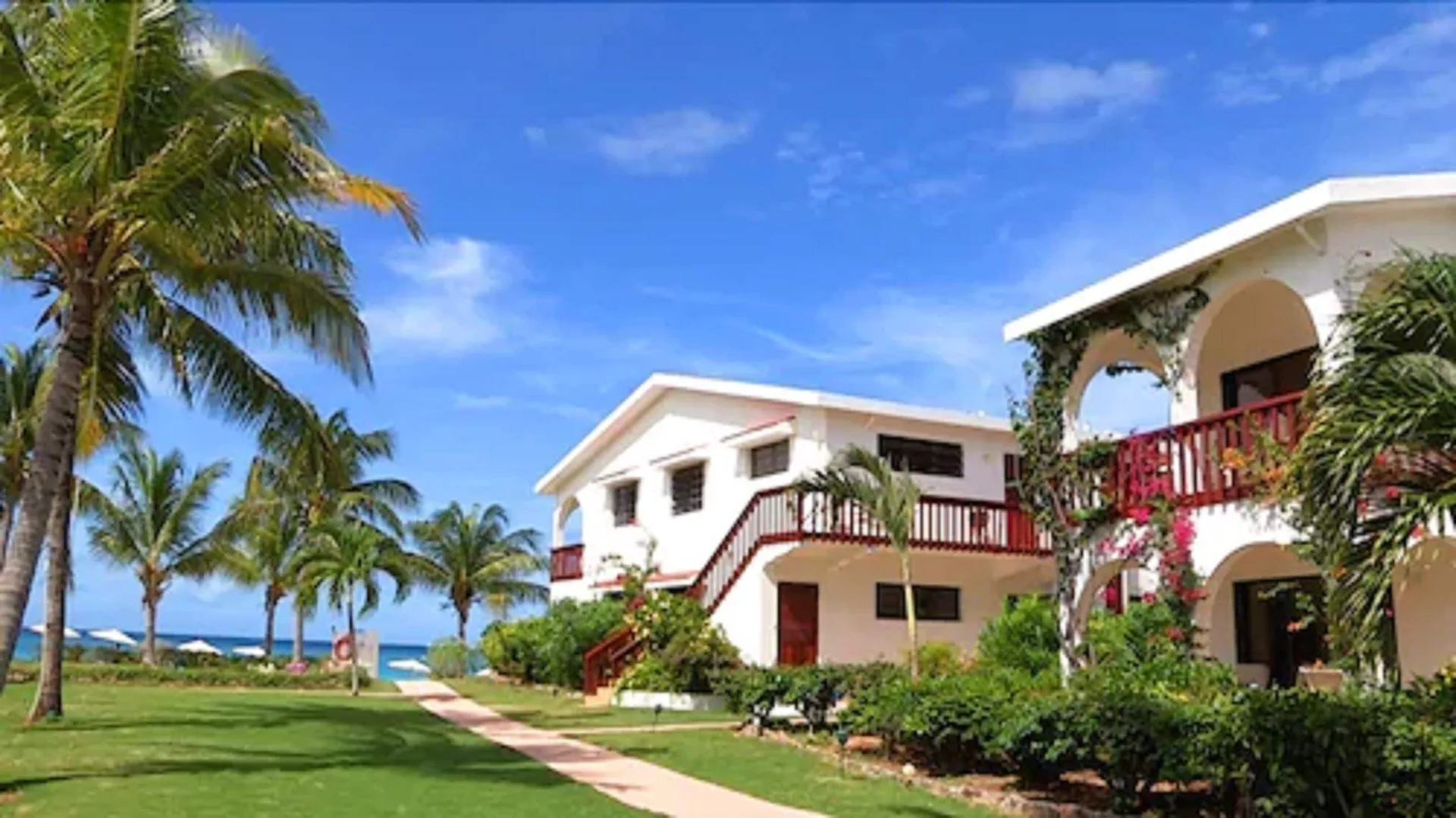 Beachfront buildings and palm-lined lawn at Carimar Beach Club under a blue sky.