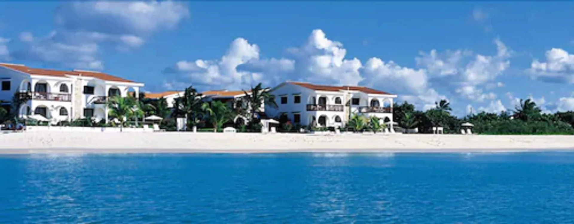 Beachfront buildings and turquoise water at Carimar Beach Club under a bright sky.