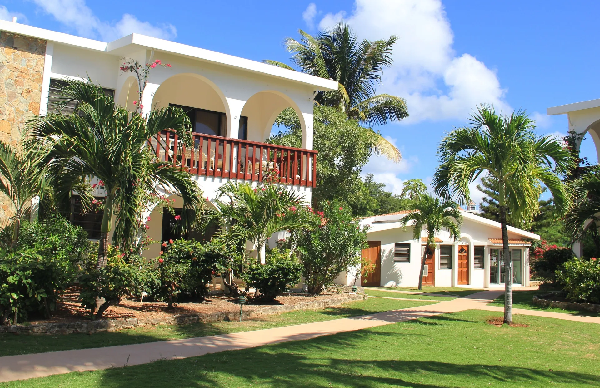 White buildings, palms, lawns, and garden paths appear at Carimar Beach Club.