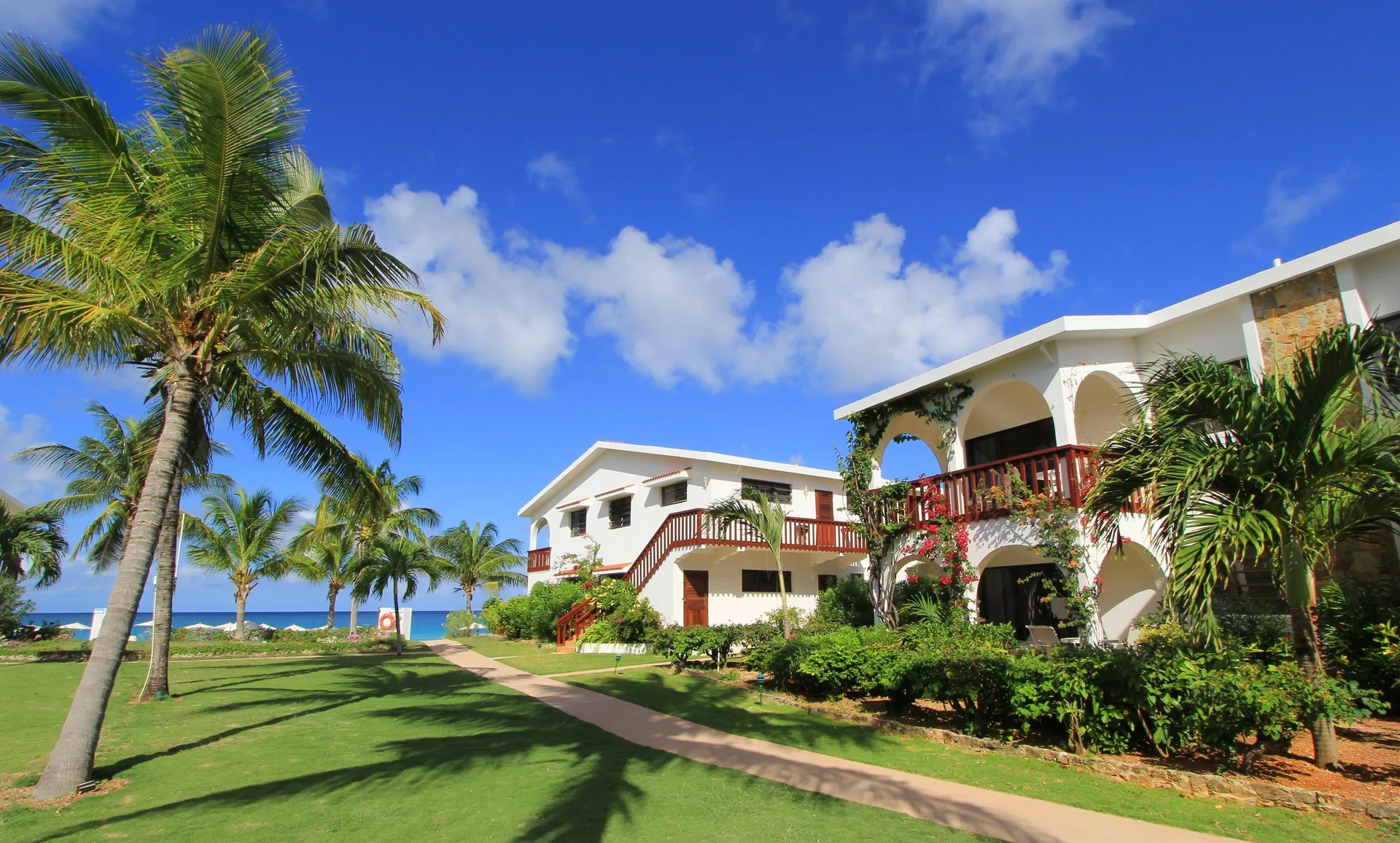 Palm lawn, walkway, and white resort buildings at Carimar Beach Club near the ocean.