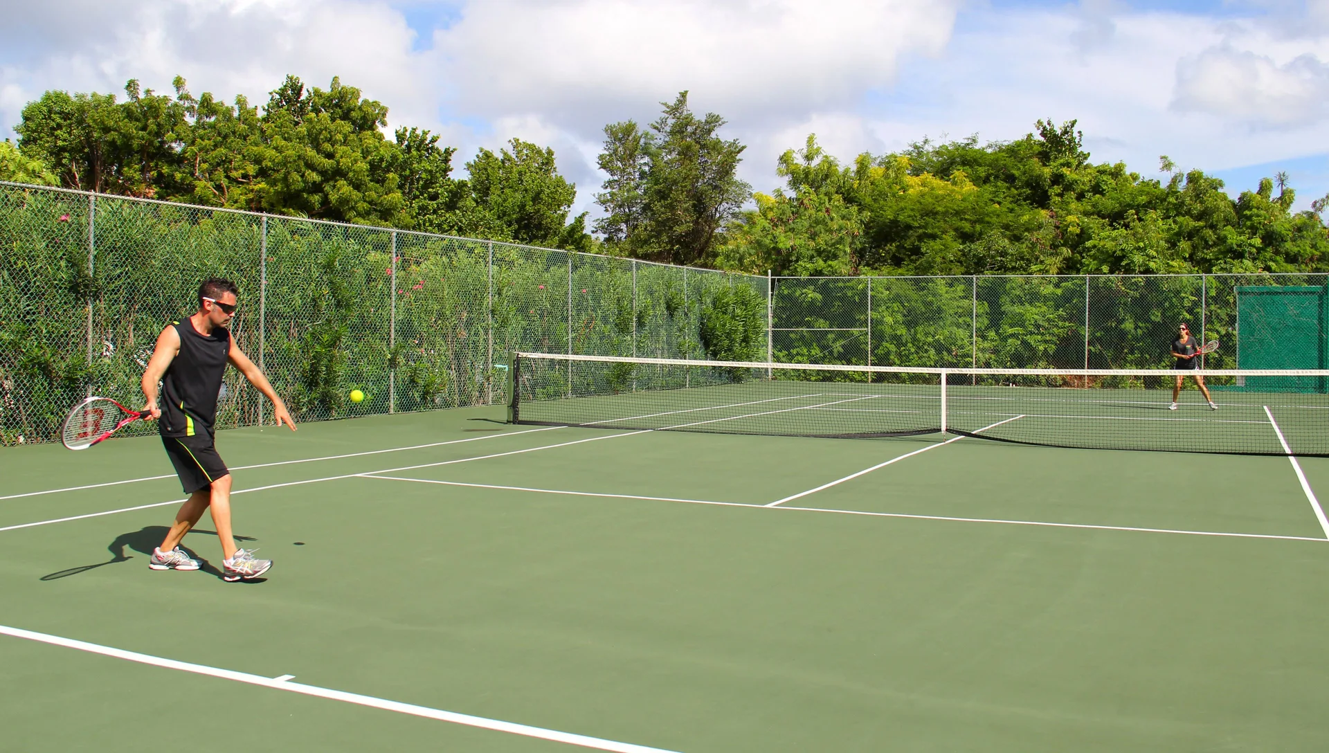 Two people play tennis on a fenced outdoor court at Carimar Beach Club.