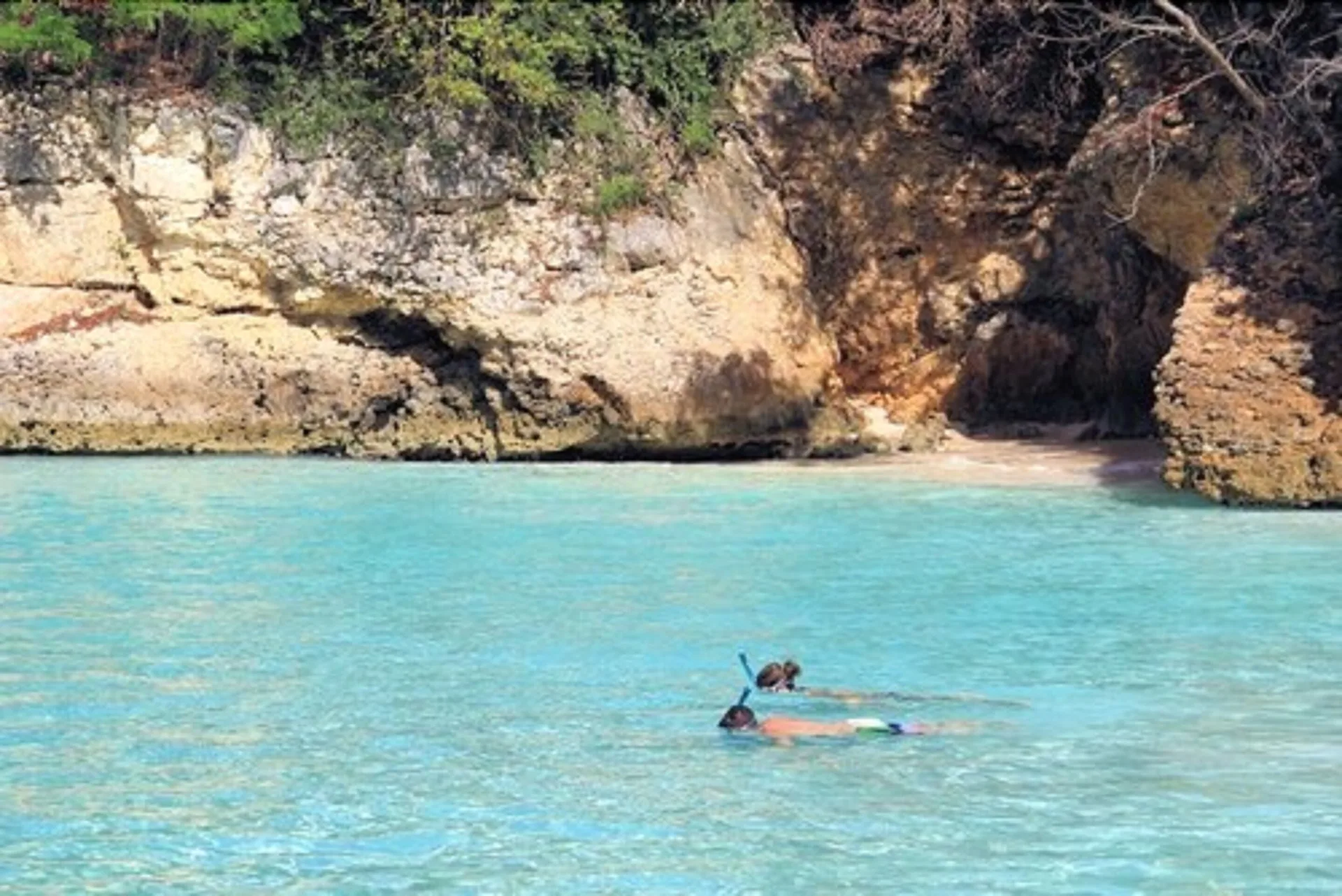 A snorkeler swims in clear turquoise water near rocky cliffs at Carimar Beach Club.