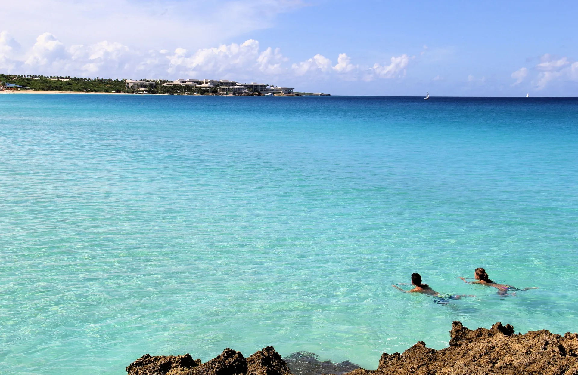 Two swimmers in bright turquoise ocean water near rocks at Carimar Beach Club.