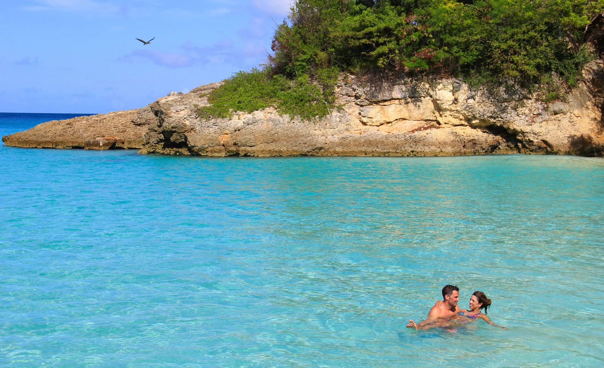 Two swimmers in clear turquoise water near a rocky shoreline at Carimar Beach Club.