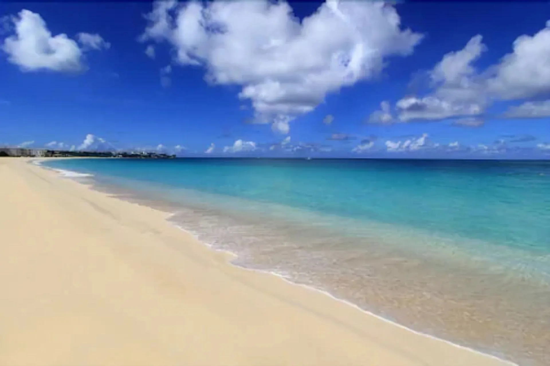 A wide sandy beach meets turquoise water under clouds at Carimar Beach Club.