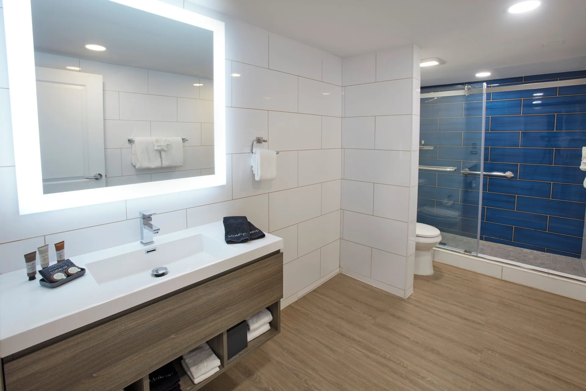 Bathroom vanity with illuminated mirror and blue-tile shower beyond at Carina Bay Boutique Resort & Casino.