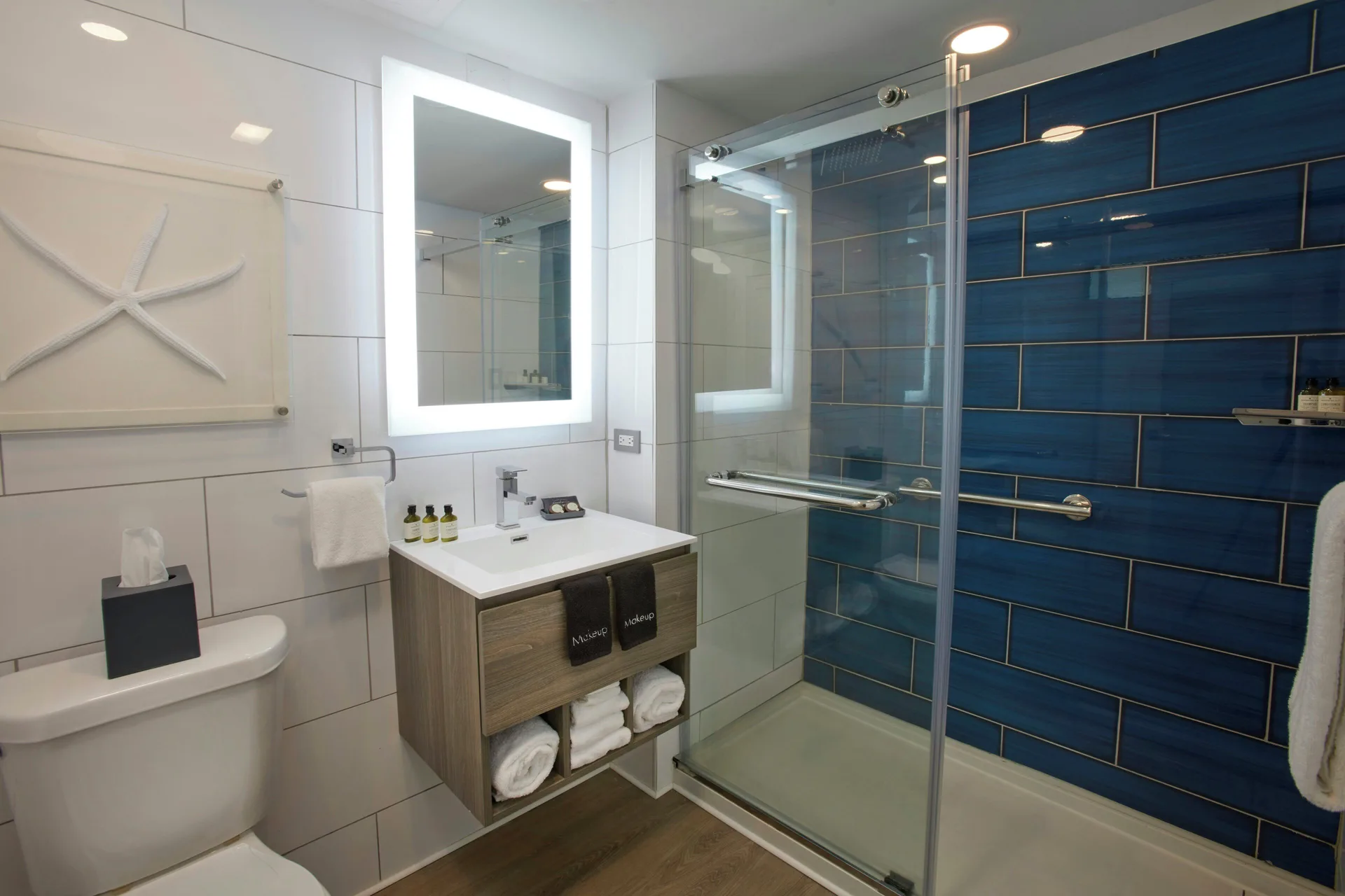 Compact bathroom with illuminated mirror and blue-tile shower at Carina Bay Boutique Resort & Casino.