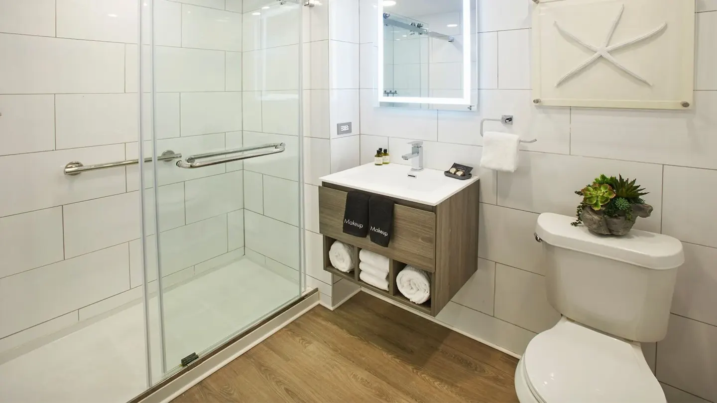 Compact guest bathroom at Carina Bay Boutique Resort & Casino with glass shower, vanity, and toilet.