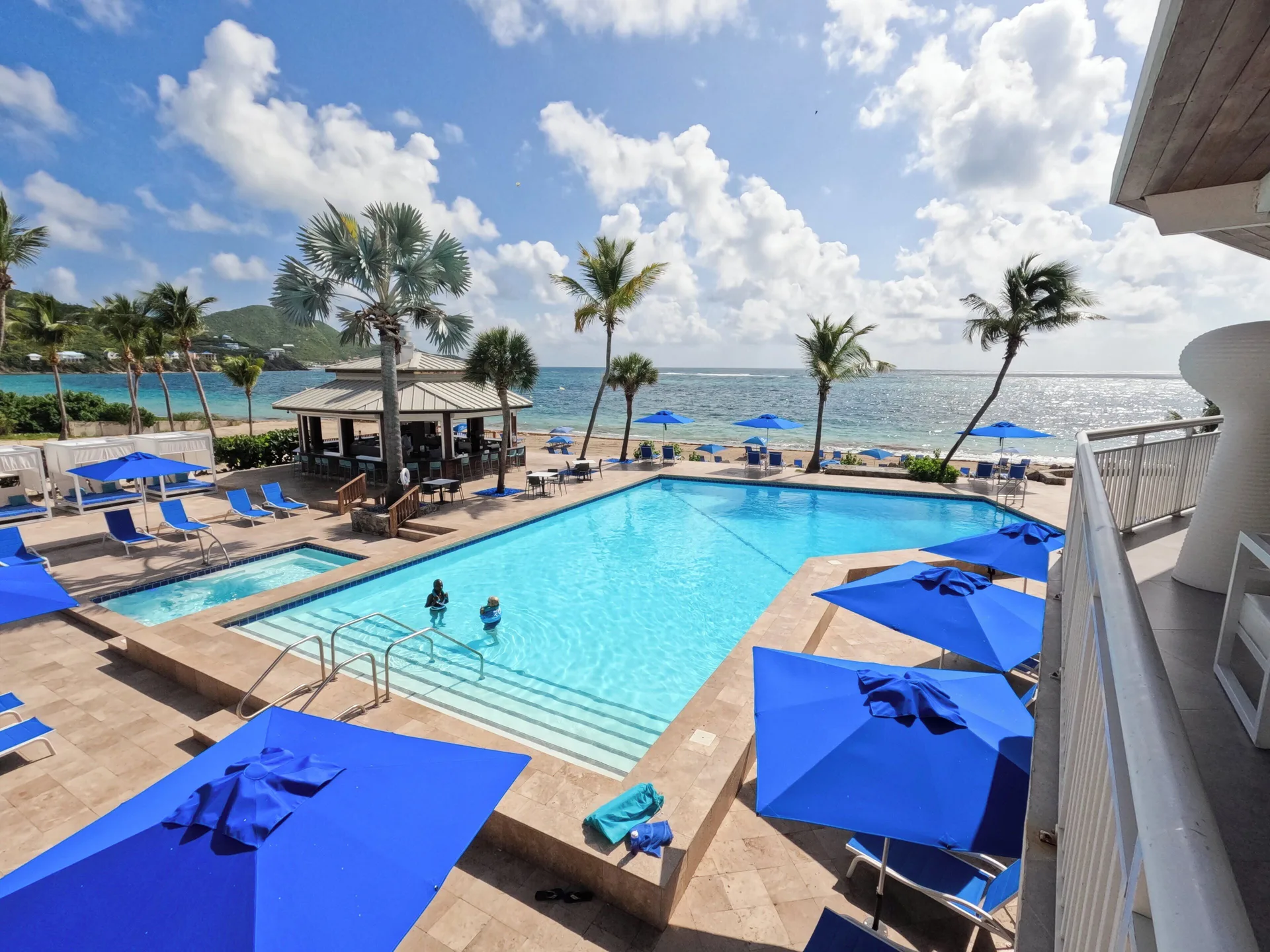 Elevated oceanfront pool view at Carina Bay Boutique Resort & Casino with blue umbrellas and palms.