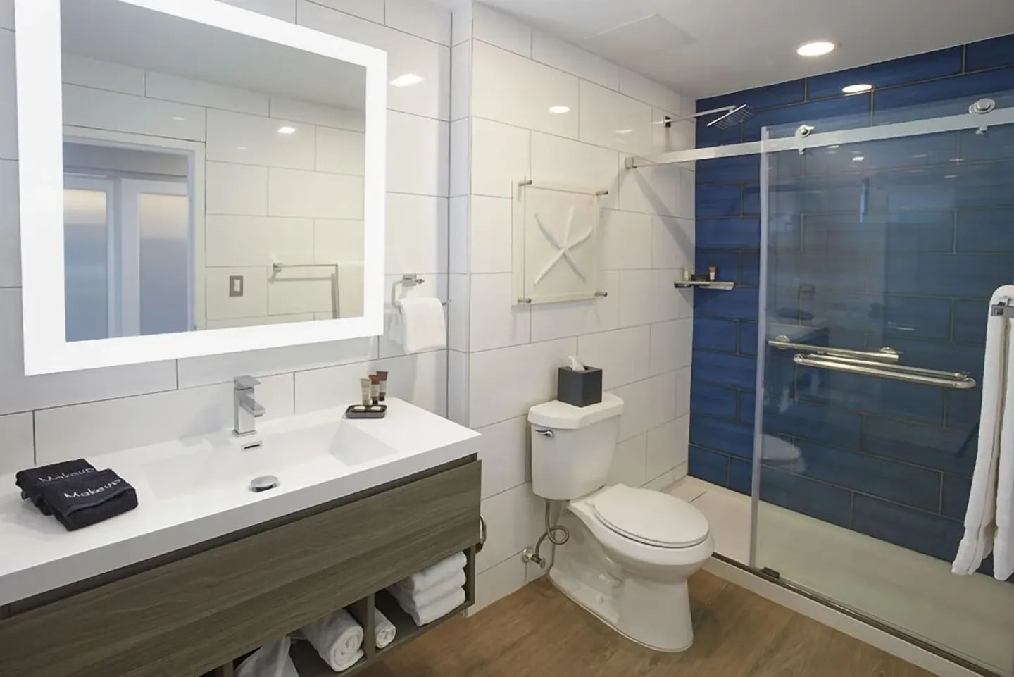 Guest bathroom at Carina Bay Boutique Resort & Casino with lit mirror, vanity, toilet, and blue-tile shower.