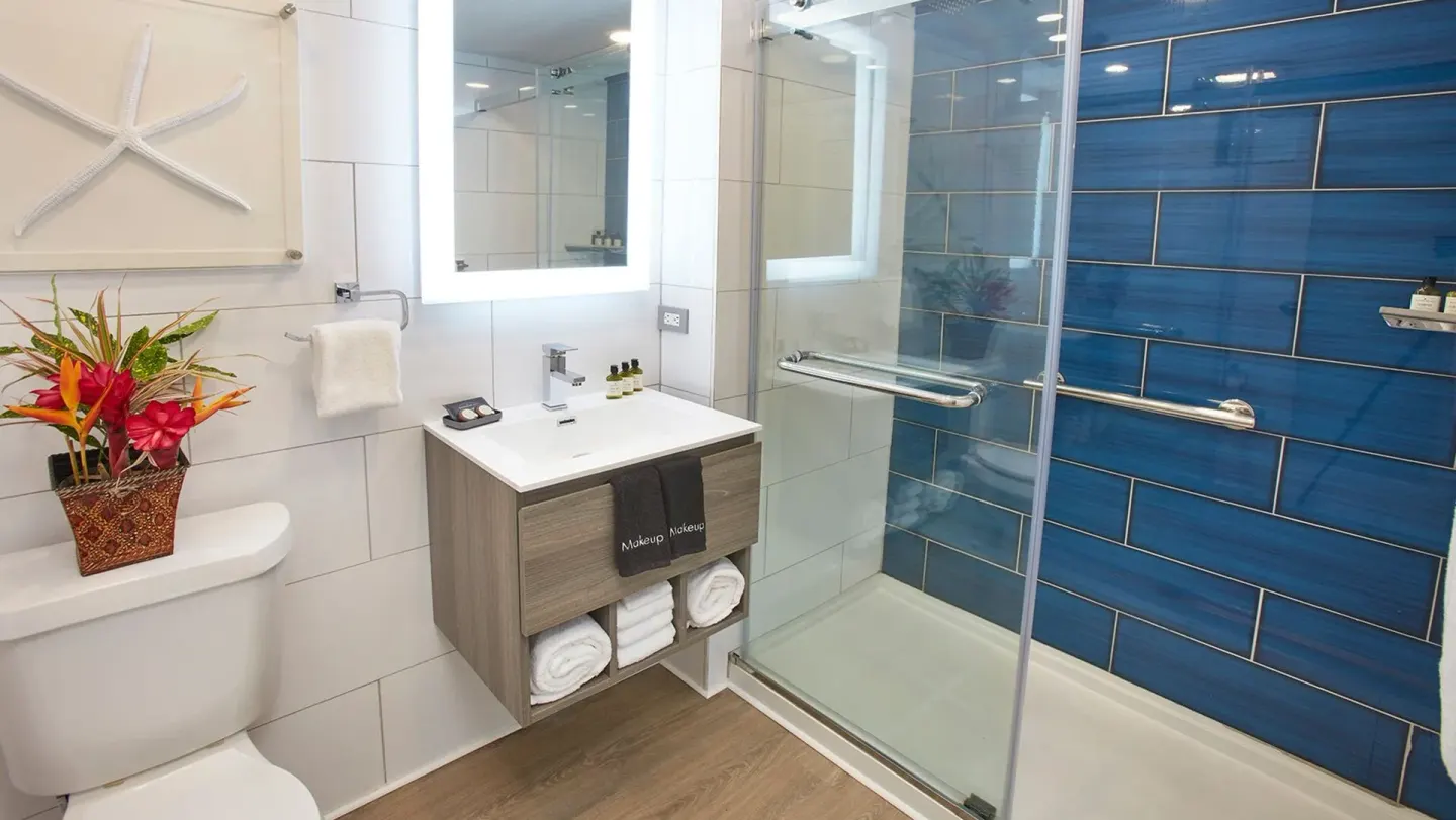 Guest bathroom at Carina Bay Boutique Resort & Casino with blue shower tile and tropical flowers.