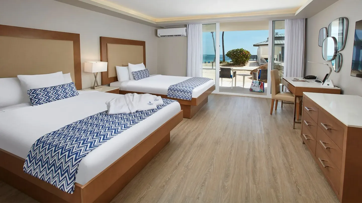 Double-bed guest room with patio and ocean beyond at Carina Bay Boutique Resort & Casino.