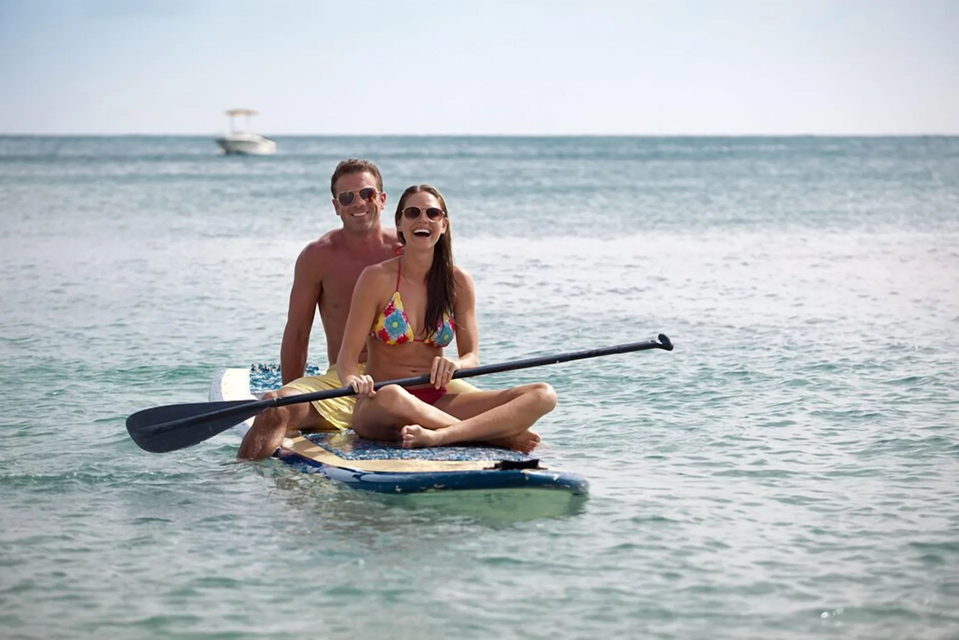 A couple sits on a paddleboard in calm water at Carina Bay Boutique Resort & Casino.