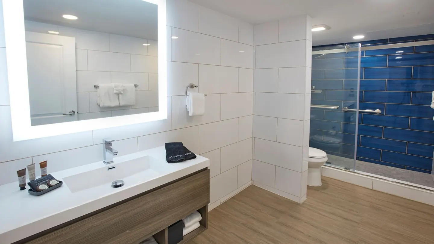 Spacious tiled bathroom with lit mirror and blue shower wall at Carina Bay Boutique Resort & Casino.