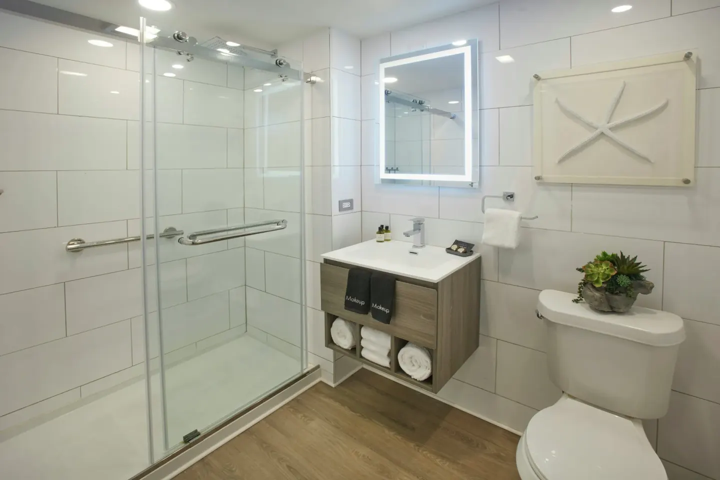 White-tile bathroom with glass shower, vanity, and starfish art at Carina Bay Boutique Resort & Casino.