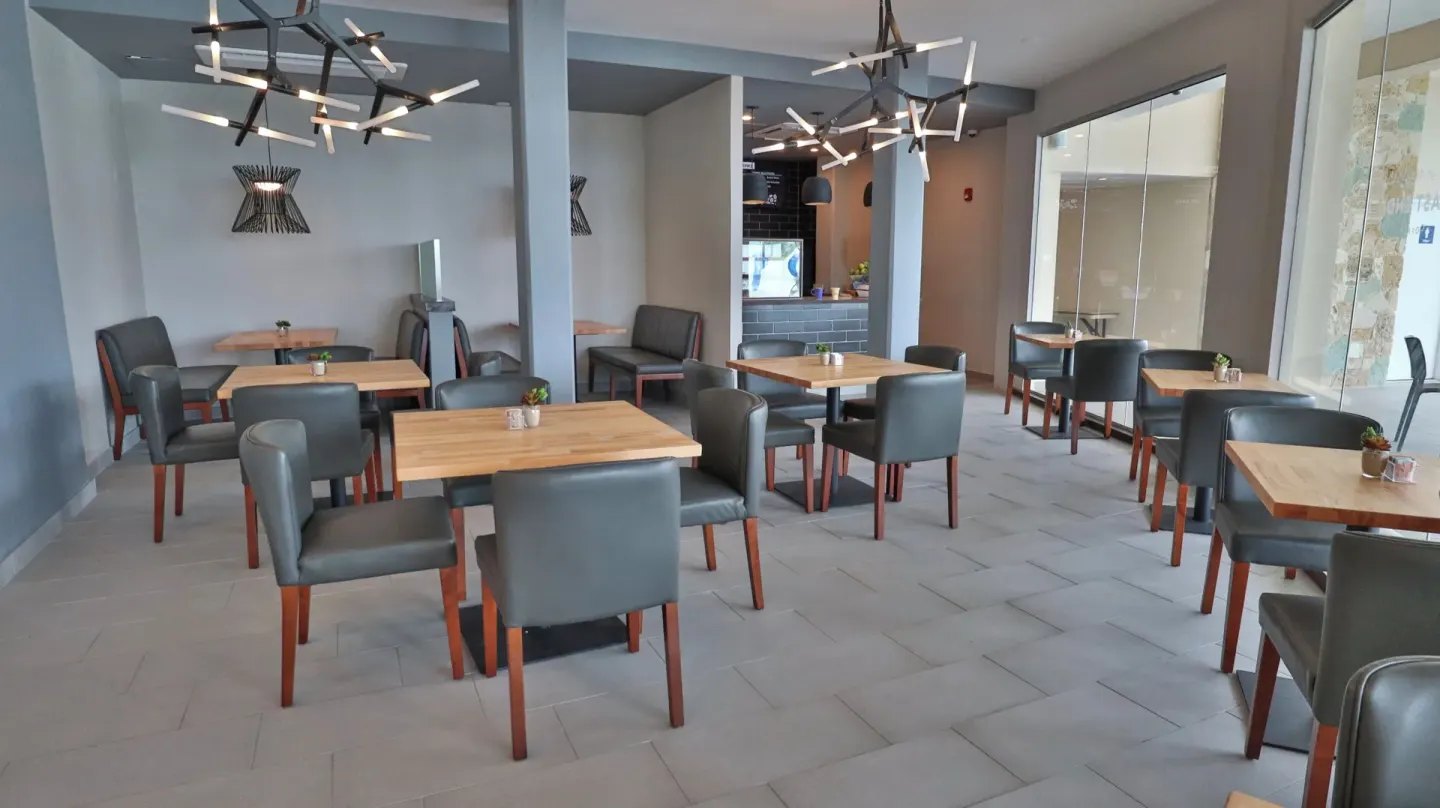 Casual dining room at Carina Bay Boutique Resort & Casino with wood tables and gray chairs.
