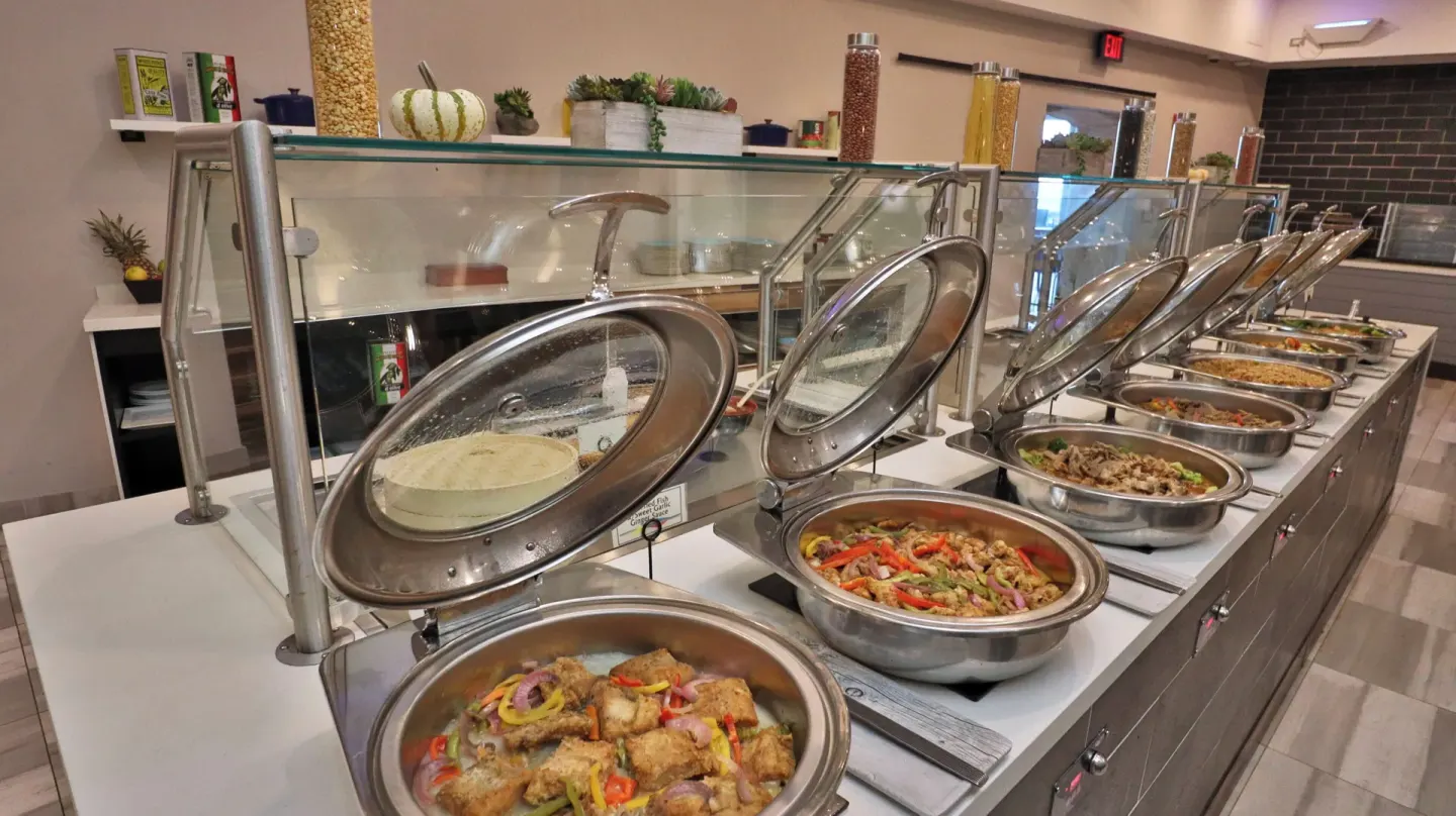 Buffet chafing dishes line a serving counter at Carina Bay Boutique Resort & Casino.