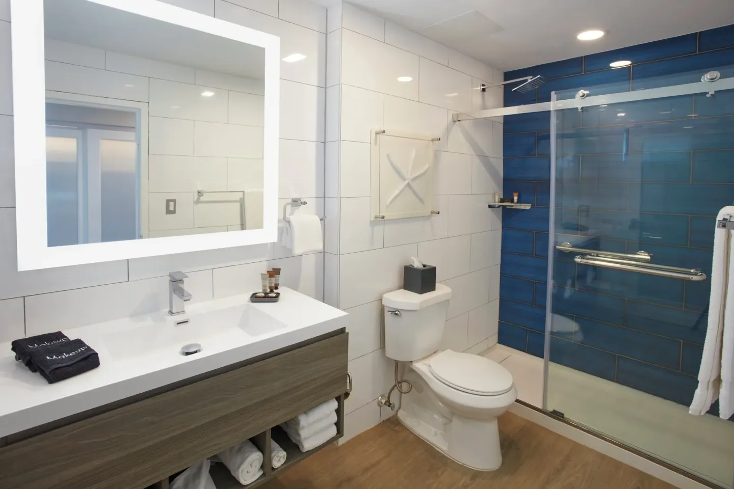 Beachfront room bathroom with lit mirror and blue-tiled shower at Carina Bay Boutique Resort & Casino.