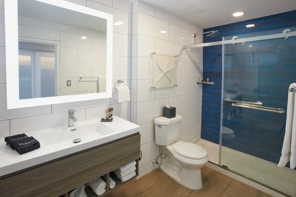 Beachfront room bathroom with lit mirror and blue-tiled shower at Carina Bay Boutique Resort & Casino.
