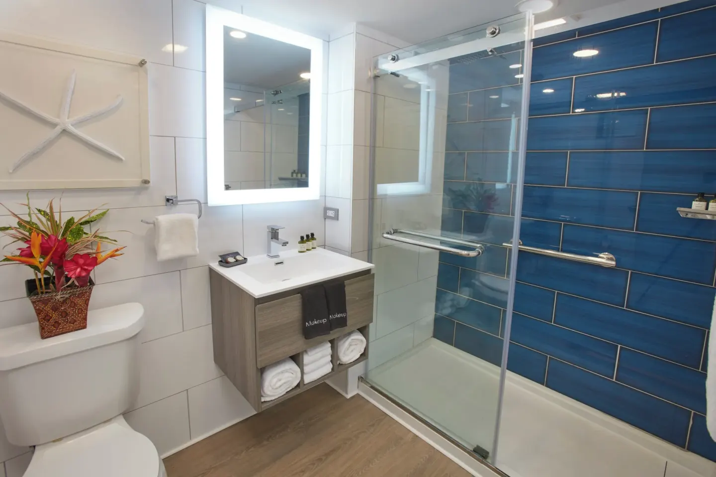 Beachfront room bathroom with vanity, glass shower, and tropical flowers at Carina Bay Boutique Resort & Casino.