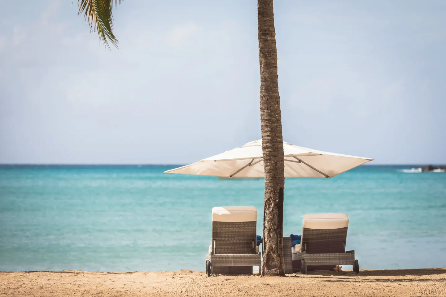 Two cushioned loungers and a white umbrella face the turquoise sea at Carlisle Bay.
