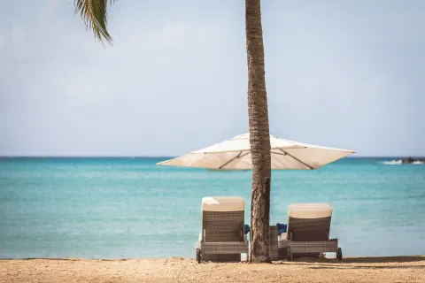Two cushioned loungers and a white umbrella face the turquoise sea at Carlisle Bay.