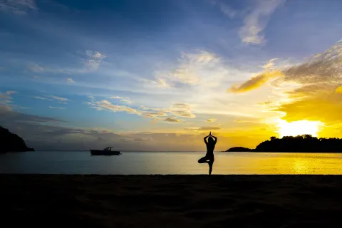 A yoga silhouette stands on the beach at sunset at Carlisle Bay.