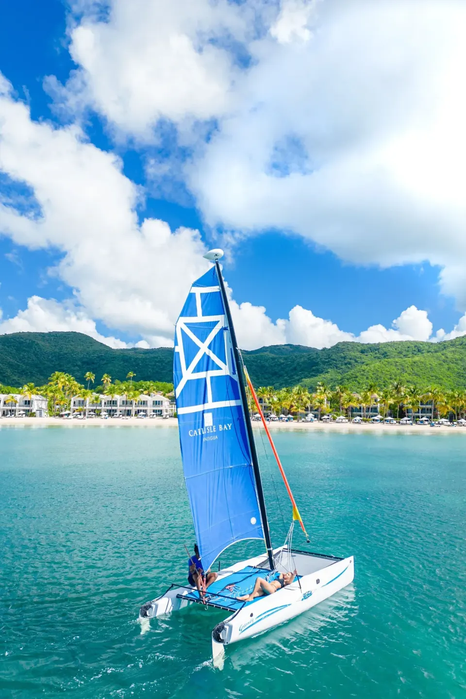 A blue-sailed catamaran glides on turquoise water off Carlisle Bay.