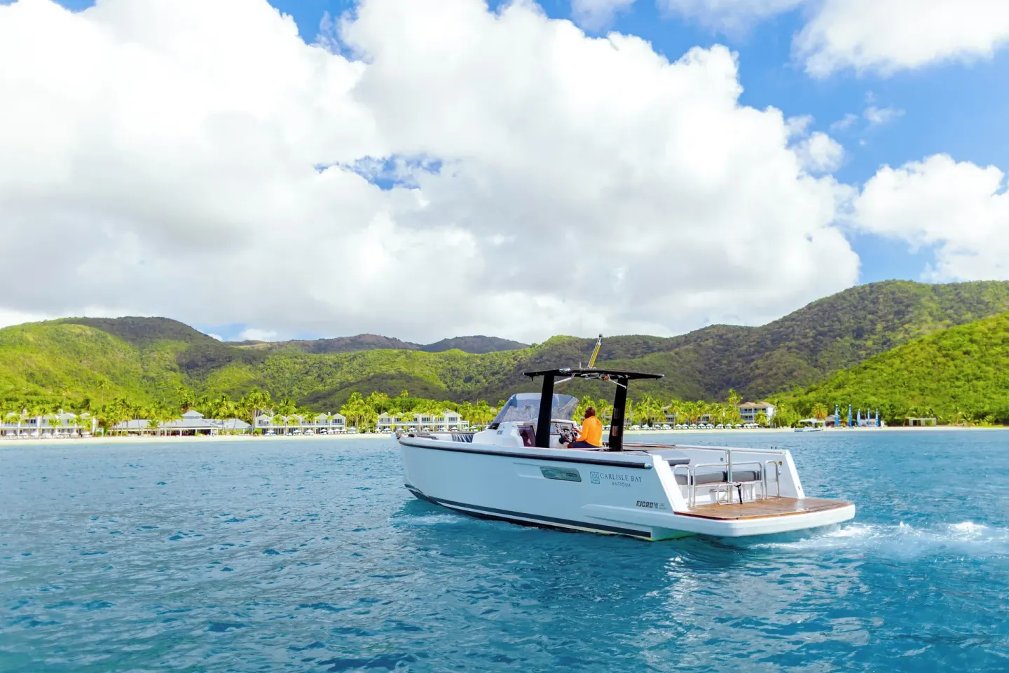 A motorboat cruises across the bay with Carlisle Bay resort in the background.