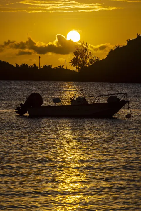 A small boat sits in silhouette on golden sunset water at Carlisle Bay.