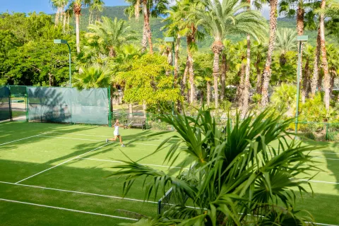 A tennis player returns a shot on a palm-lined court at Carlisle Bay.